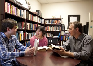 Two men, one woman sitting around circular desk discussing books in a small library.